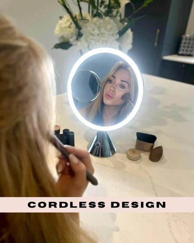 Woman using LumiGlam Pro Cosmetic Vanity Mirror in Chrome with LED lights, showcasing cordless design on vanity.