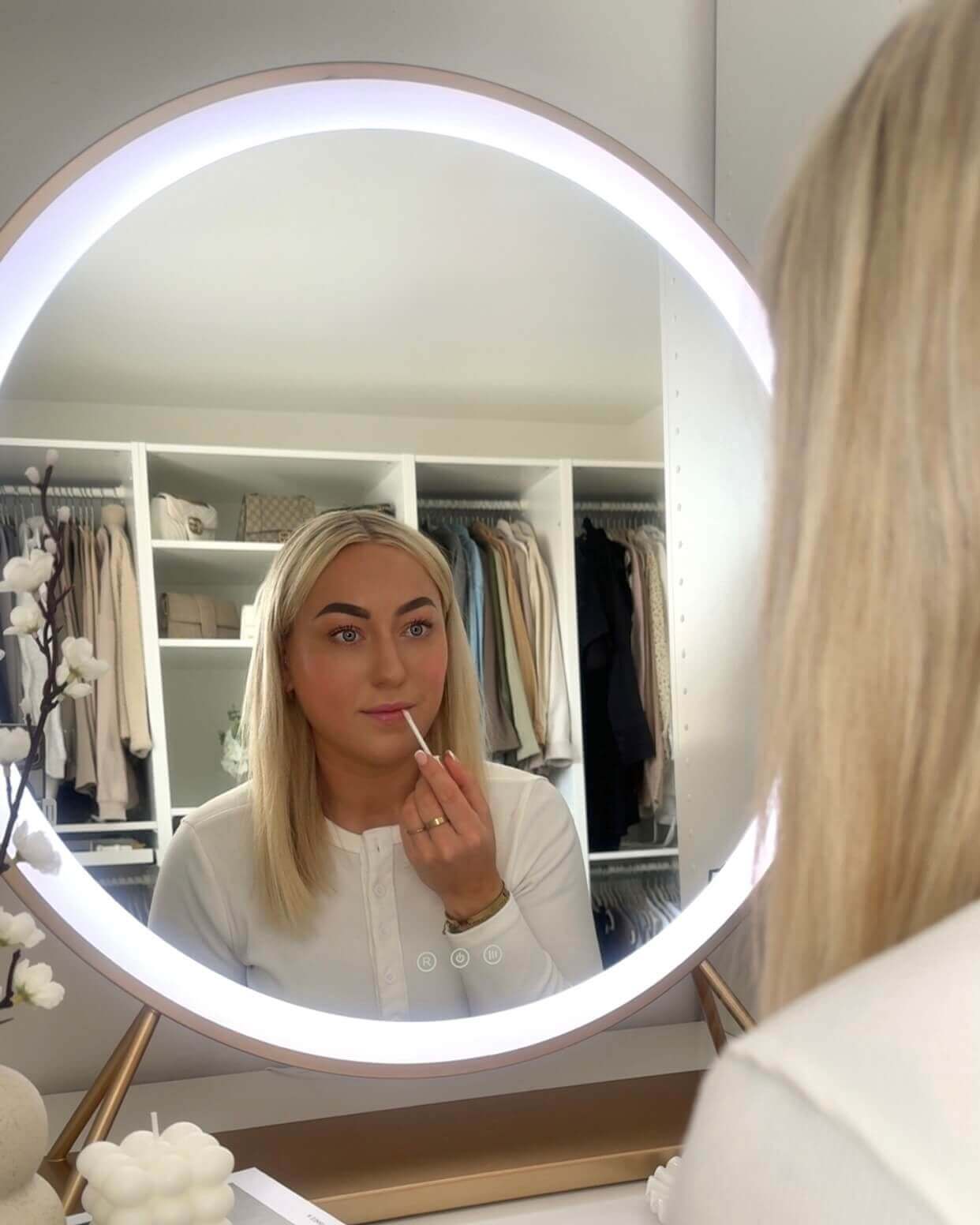 Woman applying lipstick in front of Anne Round Hollywood Mirror Gold with customizable LED lighting.