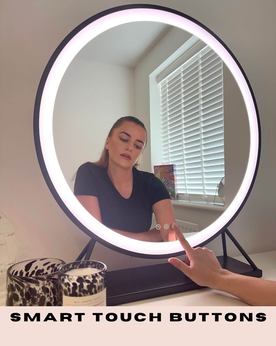 Woman using black Grace Round Hollywood Mirror with LED lighting and smart touch buttons, adding elegance to dressing room.