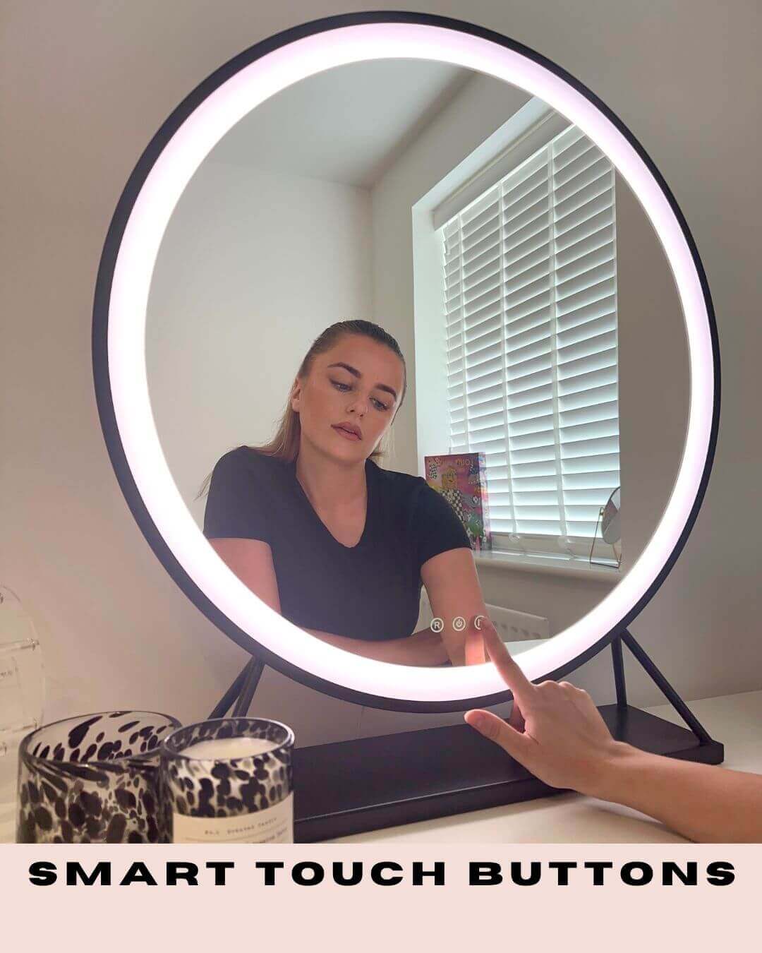 Woman using black Grace Round Hollywood Mirror with LED lighting and smart touch buttons, adding elegance to dressing room.