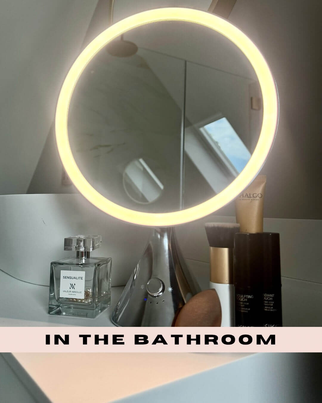 LumiGlam Pro Cosmetic Vanity Mirror in chrome with LED light on bathroom counter, surrounded by perfume and makeup products.