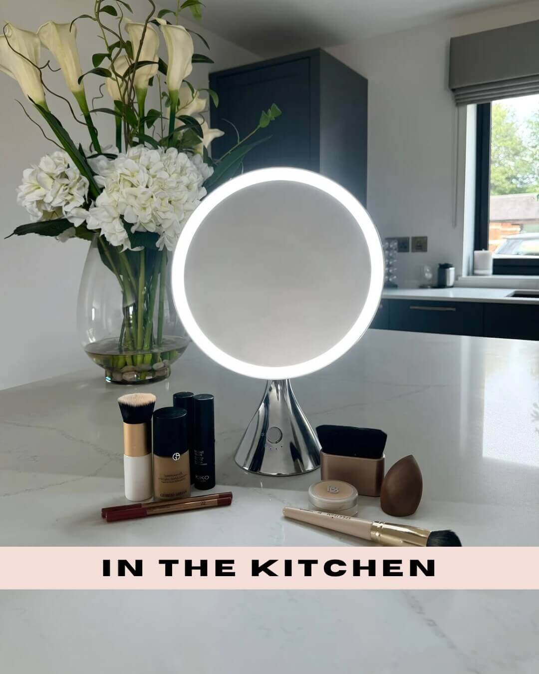 LumiGlam Pro Vanity Mirror in chrome with LED lights, surrounded by makeup, on marble kitchen countertop with flowers.