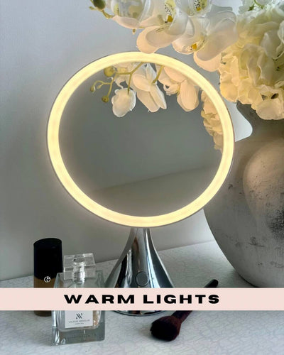 LumiGlam Pro Vanity Mirror in Chrome with warm LED lights, surrounded by flowers, cosmetics, and a makeup brush.