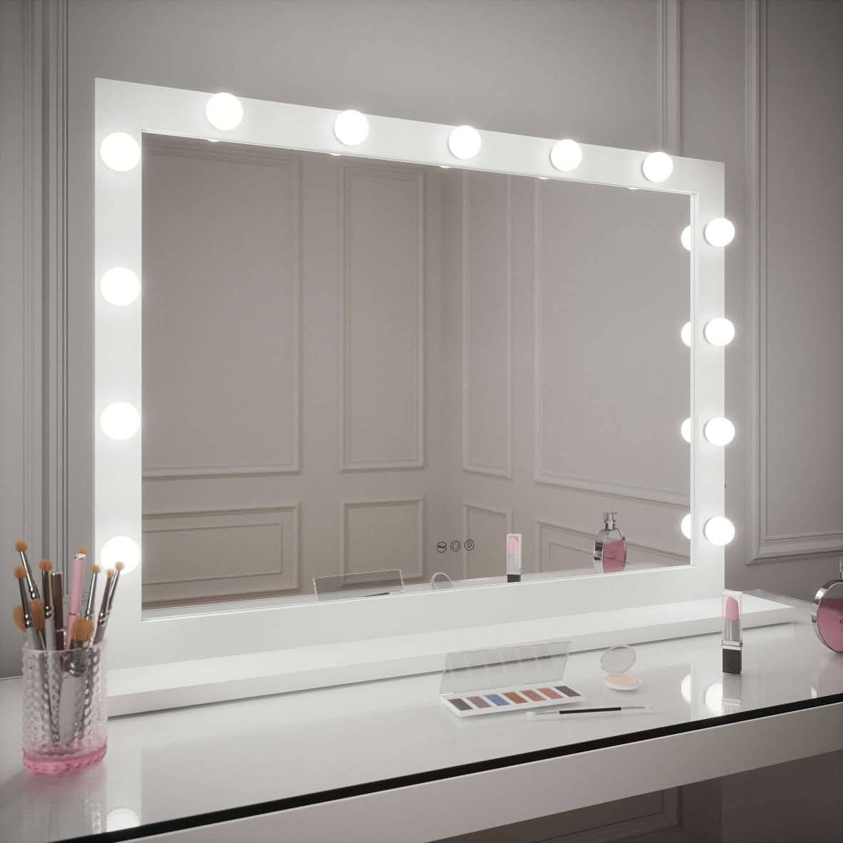 The Audrey Hollywood Mirror White 100x80cm by hollywood mirrors features a large, studio-lit frame. On the elegant table: makeup brushes in glass, an eyeshadow palette, powder, lipstick, and a small pink clock complete the minimal setup.