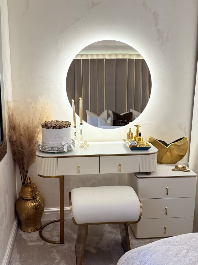 Dressing table with round mirror, candles, and decorative items in a bedroom setting.