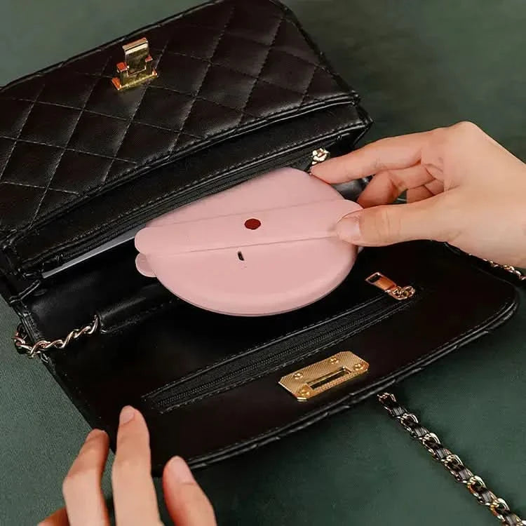 Compact light pink handheld flip mirror with LED lights being placed into a black quilted handbag.