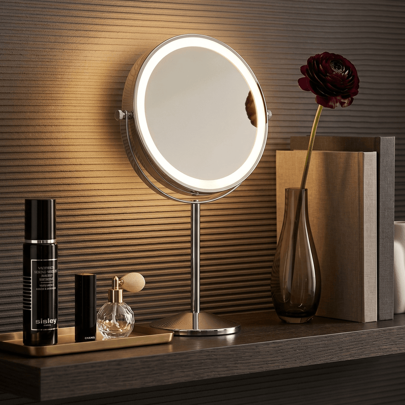 Small round mirror with lights on a wooden surface next to skincare products and a rose.