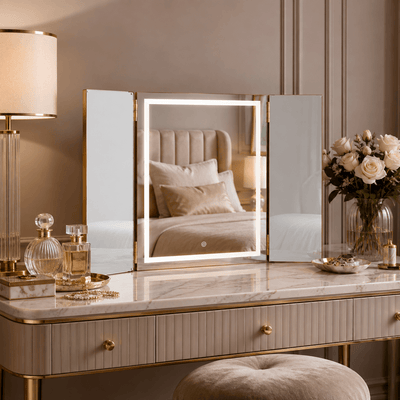 Gold LED trifold vanity mirror styled with perfume and beauty accessories