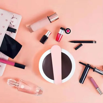 Hand Held Flip Mirror with Light in pink surrounded by cosmetics on a peach background.