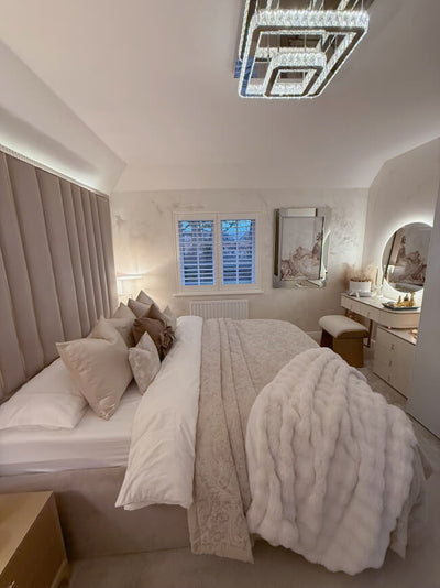 Neatly made bed in a bedroom with a window and vanity area.
