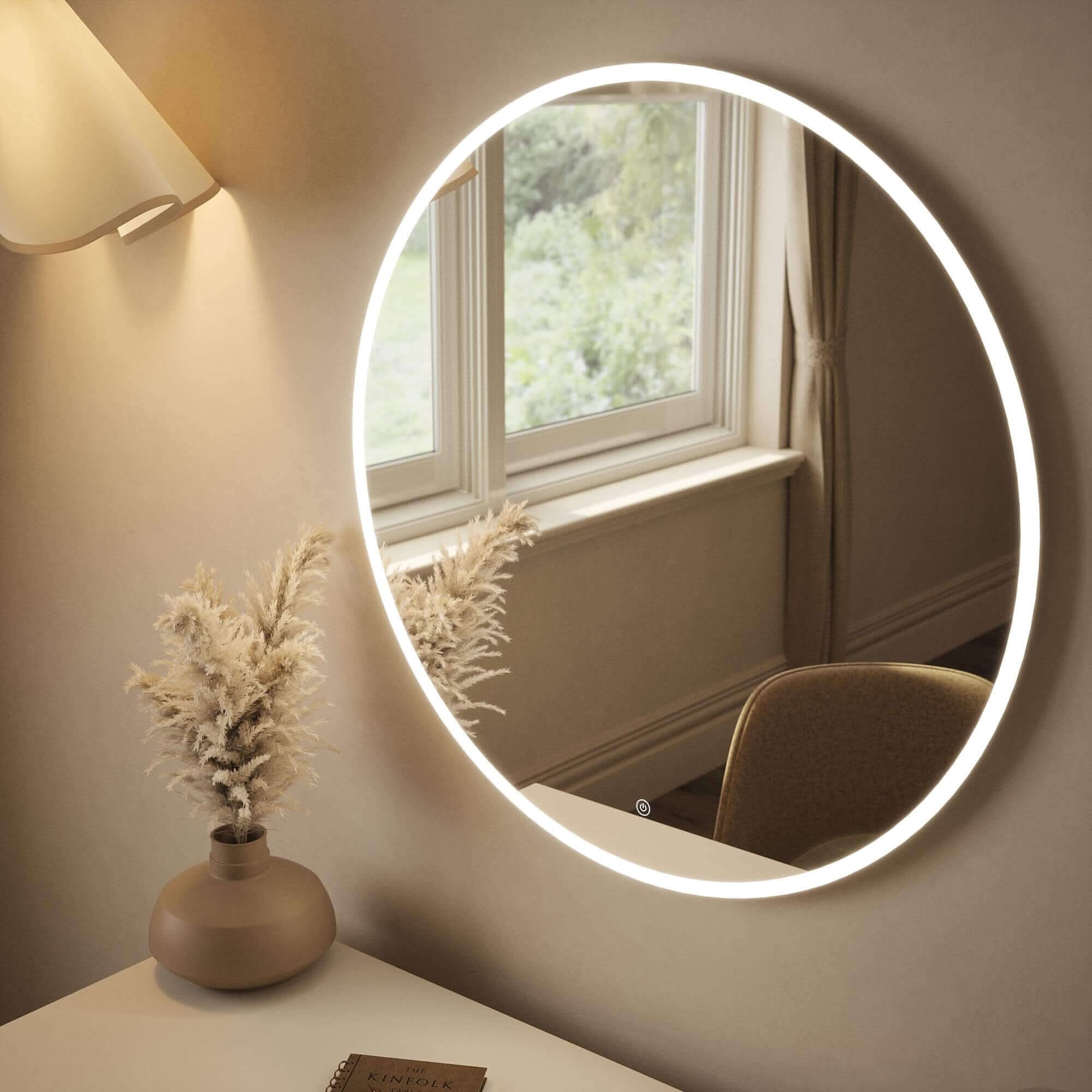 Round backlit mirror with ambient lighting on a wall above a desk, featuring a window reflection and decorative vase.