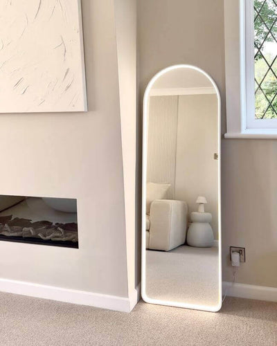 Sophia Full Length Arch Mirror White Frame with LED lighting, leaning against a beige wall in a modern living room.