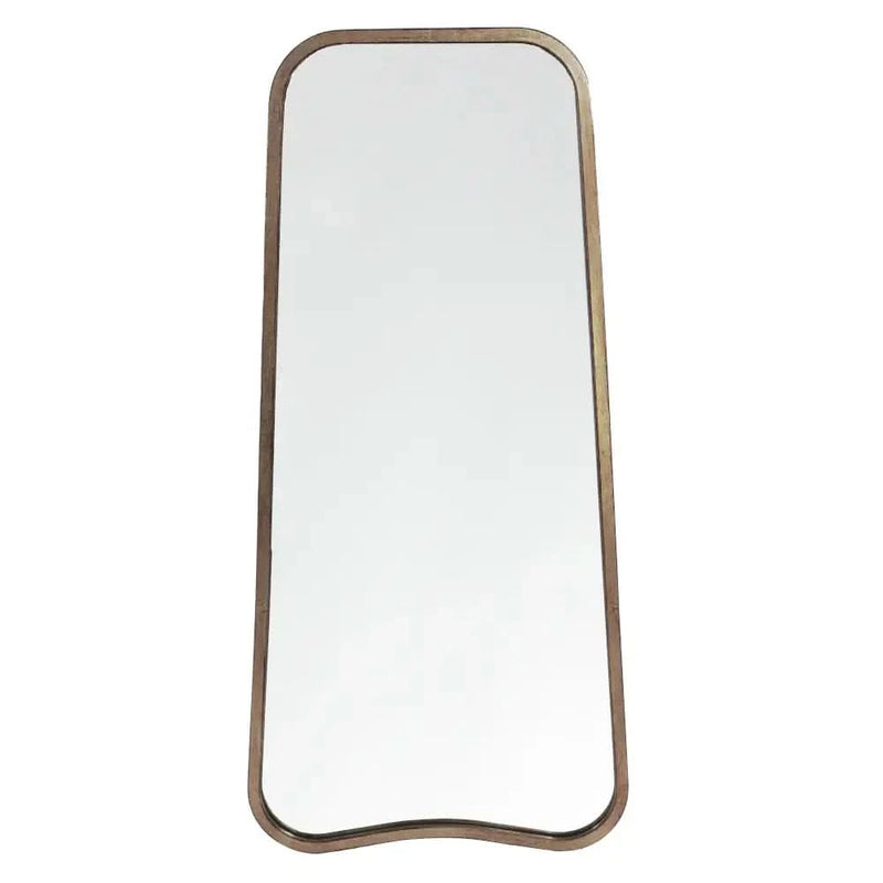 The hollywood mirrors Valentina Gold Full Length Mirror (123cm x 56.5cm) leans against a beige wall, its unique shape reflecting a small table with a vase, while a dark blue velvet chair sits nearby.