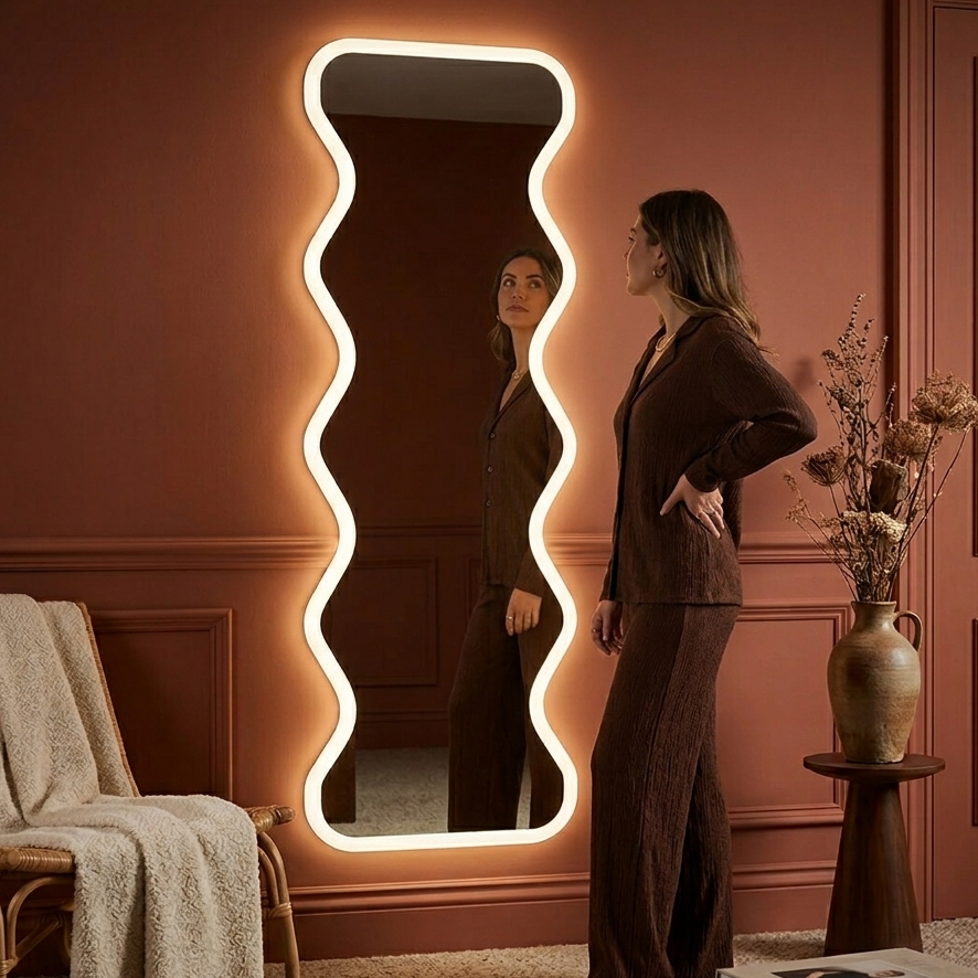 Woman standing in front of a decorative mirror with wavy frame in a room with a pink wall.