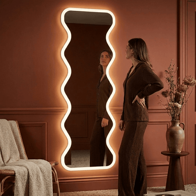 Woman standing in front of a decorative mirror with wavy frame in a room with a pink wall.