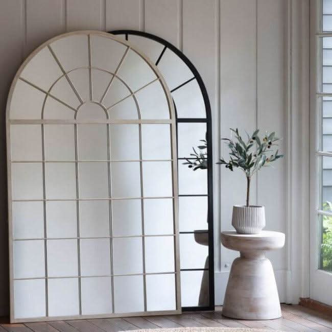 Silver Hemsworth leaner mirror with arched window pane style, elegantly leaning against a wall next to a modern plant stand.
