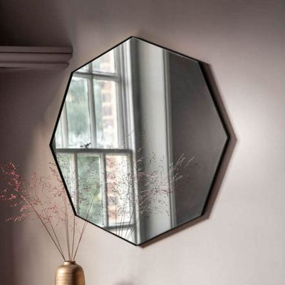 Black Octagon Bowie Mirror with sleek angled frame and silver surround, hanging on a wall near a window, reflecting modern style.
