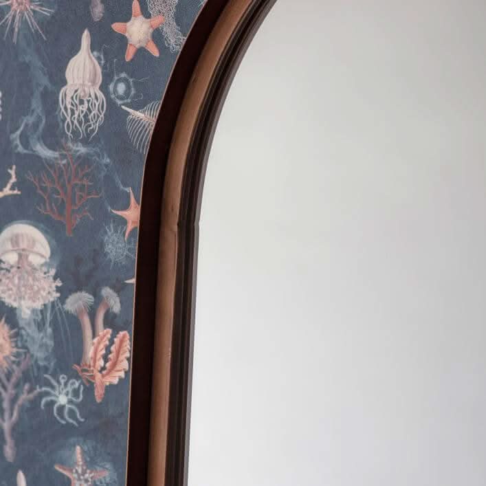 Bronze Arch Leaner Mirror 170x51cm in modern living room with blue chair, floral wallpaper, and wood paneling.