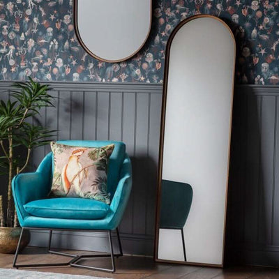 Bronze Arch Leaner Mirror 170x51cm in modern living room with blue chair, floral wallpaper, and wood paneling.