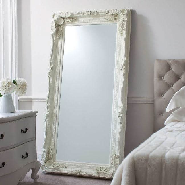 Charles leaner mirror in cream with elegant wood and resin frame, carved details, displayed in a chic bedroom setting.