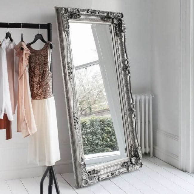 Elegant Charles Silver Leaner Mirror with decorative frame, leaning against a wall, reflecting light in a stylish room.