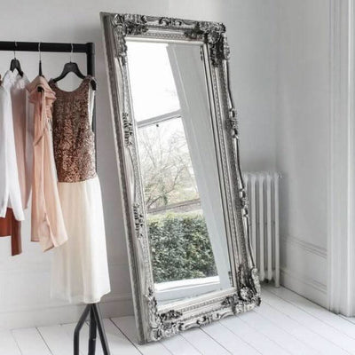 Elegant Charles Silver Leaner Mirror with decorative frame, leaning against a wall, reflecting light in a stylish room.