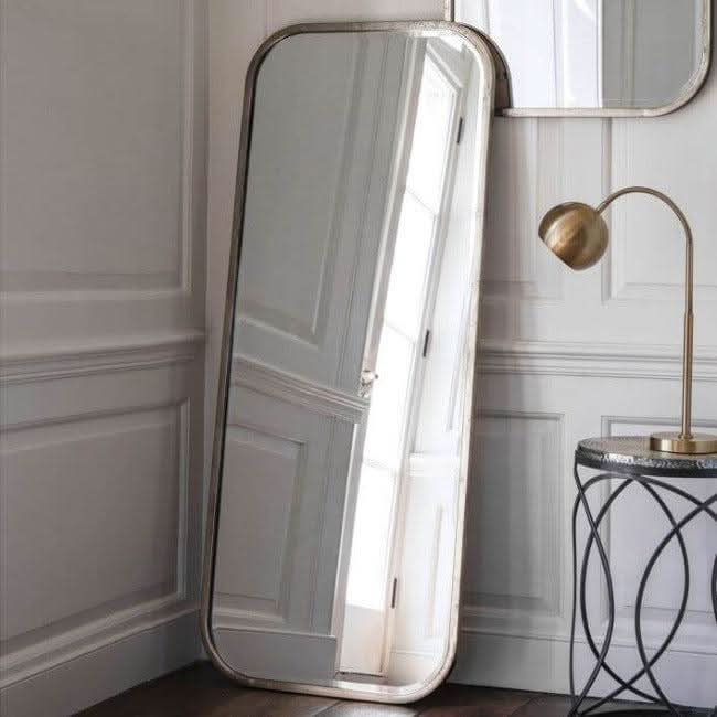 Distressed Champagne Leaner Mirror with streamlined metal frame, enhancing elegant home décor next to a brass lamp.