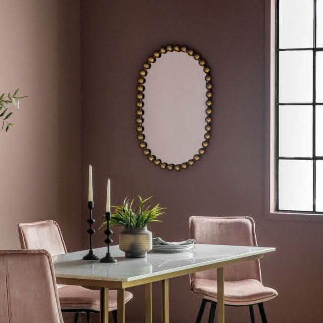 Gold Pill mirror with oversized beading and bold black finish hanging in modern dining room with pink chairs and table.