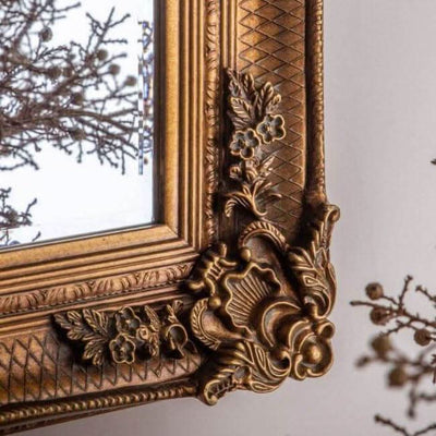Close-up of baroque-style mirror with handcrafted gold leaf wood frame featuring ornate floral details, suitable for horizontal or vertical hanging.