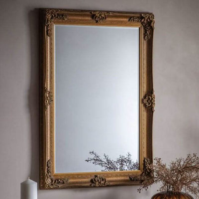 Baroque-style handcrafted wood framed mirror with gold leaf finish, hanging vertically on a wall.