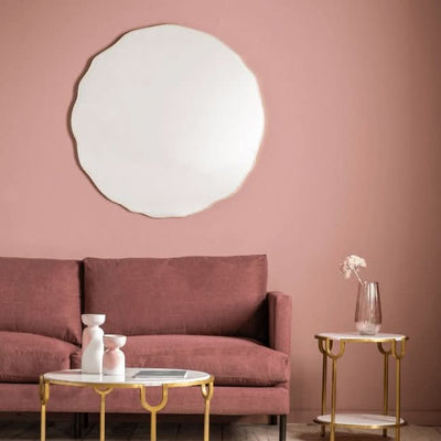 Large round champagne mirror with elegant metal frame above a pink sofa, adding modern sophistication and light to the room.