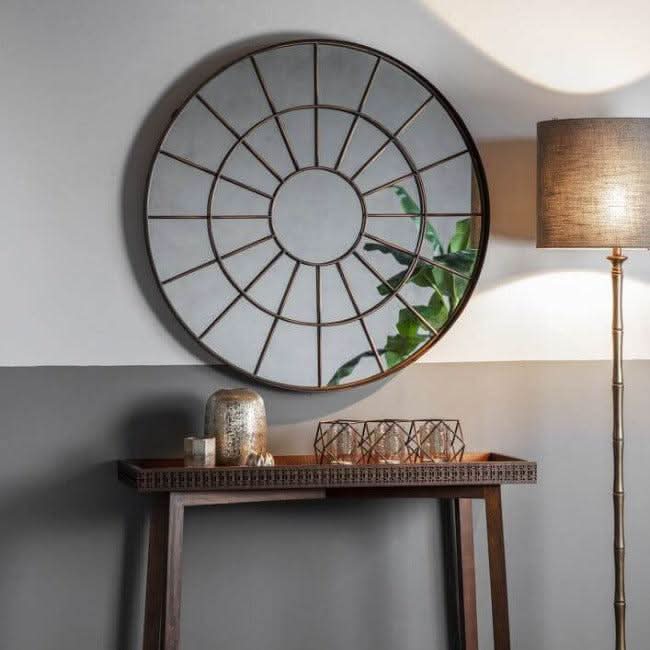 Large round chic industrial window mirror with bronzed metal frame, hanging on a wall above a console table, adding rustic charm to the room.