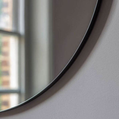Close-up of Scandi Large Round Mirror with slim black metal frame, near window, showcasing modern industrial design, 80cm diameter.