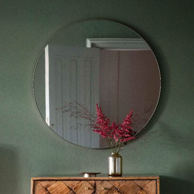 Scandi large round mirror with silver metal frame, 80cm, on a wall above a wooden cabinet featuring a vase with red flowers.