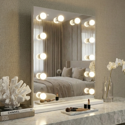 Makeup vanity with mirror and lights, featuring a bed in the reflection.