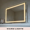 The Hollywood Crystal Pro Mirror 80x60cm by hollywood mirrors features a built-in warm LED strips border and is shown wall-mounted above a white surface with a decorative vase. WARM LIGHTS appears at the bottom of the image.