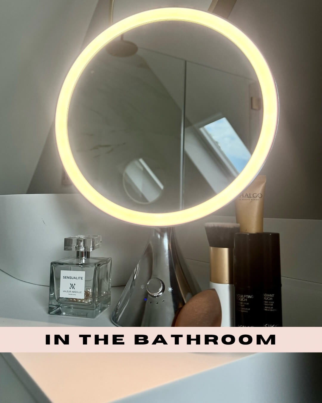 LumiGlam Pro Cosmetic Vanity Mirror in chrome with LED light on bathroom counter, surrounded by perfume and makeup products.