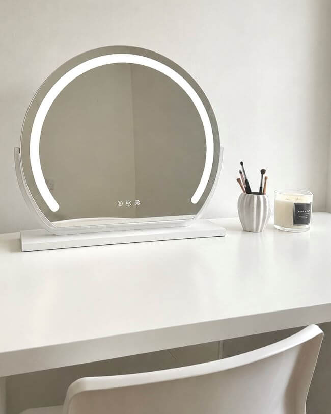 Round illuminated mirror on a wooden console table with decorative items against a dark wall.