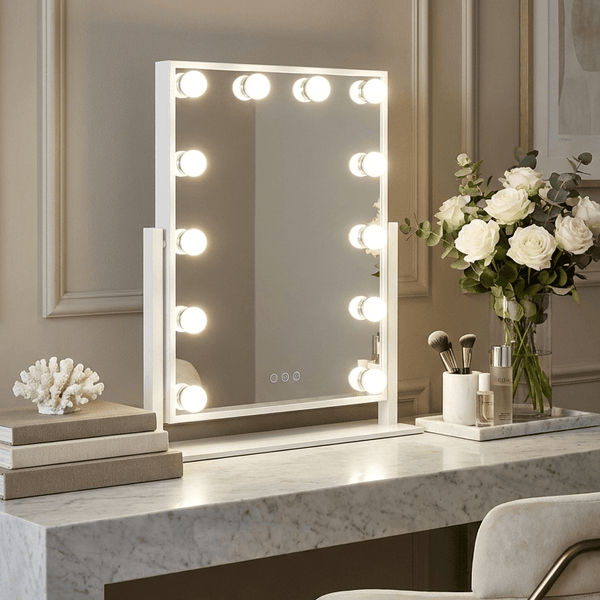 Makeup vanity with a mirror with lights, books, a vase of flowers, and a chair.