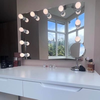 The Penelope Hollywood Mirror Wall Mounted 80cmx60cm, with LED bulbs and a sleek vanity table by the window, creates an ideal setup for any makeup artist—combining style, storage, and perfect lighting.