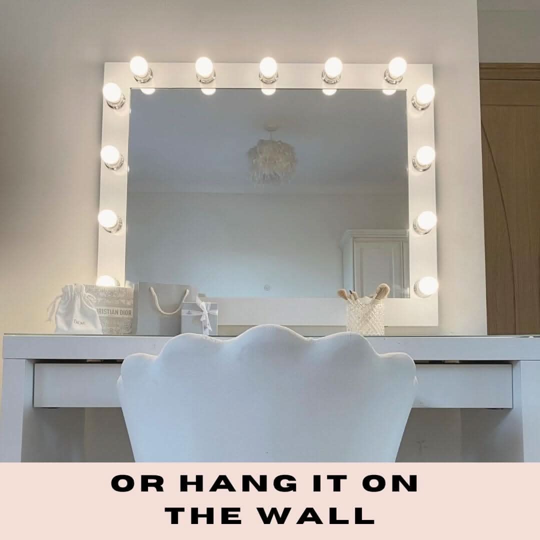 The Audrey Hollywood Mirror White 100x80cm by hollywood mirrors sits on a white vanity with a scalloped chair, framed by Tri-Colour LED Bulbs. Makeup and a small bag are on the table. Text at the bottom: OR HANG IT ON THE WALL.