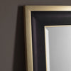 Close-up of the top left corner of the Hollywood Mirrors Hudson Black & Gold Full Length Mirror—a rectangular design with bevelled glass and a wide, two-tone frame featuring a brushed gold edge and sleek black inner panel against a gray wall.
