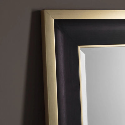 Close-up of the top left corner of the Hollywood Mirrors Hudson Black & Gold Full Length Mirror—a rectangular design with bevelled glass and a wide, two-tone frame featuring a brushed gold edge and sleek black inner panel against a gray wall.
