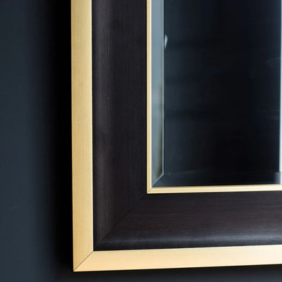 Close-up of the Hudson Black & Gold Full Length Mirror by Hollywood Mirrors, featuring a rectangular design with bevelled glass, sleek black frame, and gold metal border, reflecting part of a dark wall.