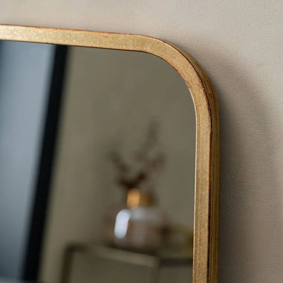 Close-up of The Valentina Gold Mirror Full Length Mirror by hollywood mirrors (123cm x 56.5cm), a rectangular design with a gold frame and rounded corners, reflecting a blurred decorative object against a neutral wall.
