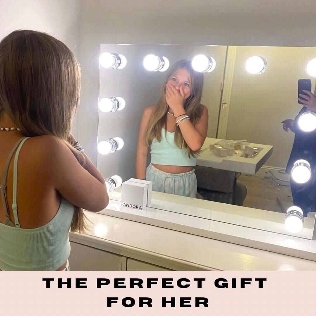 Woman admiring herself in a brightly lit Hollywood mirror, joyful expression, labeled 'The Perfect Gift for Her.'