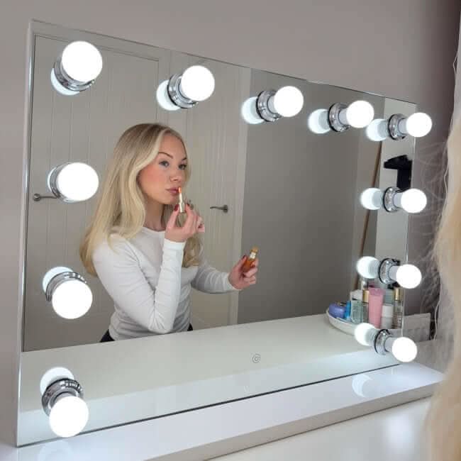 Woman applying makeup in front of Hepburn Hollywood Mirror with LED lighting, showcasing a chic, glamorous setup with freestanding design.