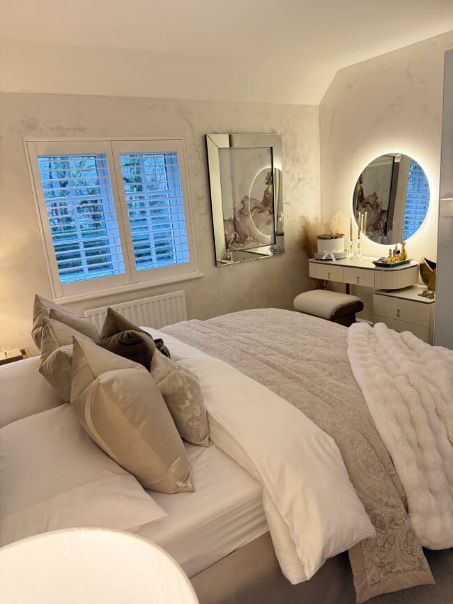 Neatly made bed in a bedroom with decorative pillows and a mirror.