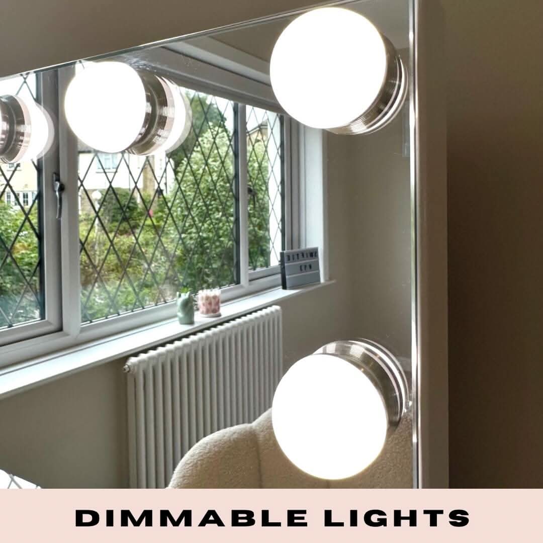 A close-up of the Jessica Hollywood Mirror 58cmX46cm with large round LED bulbs and versatile lighting, reflecting a window with diamond-patterned glass, a radiator, and a white chair. “DIMMABLE LIGHTS” appears at the bottom.