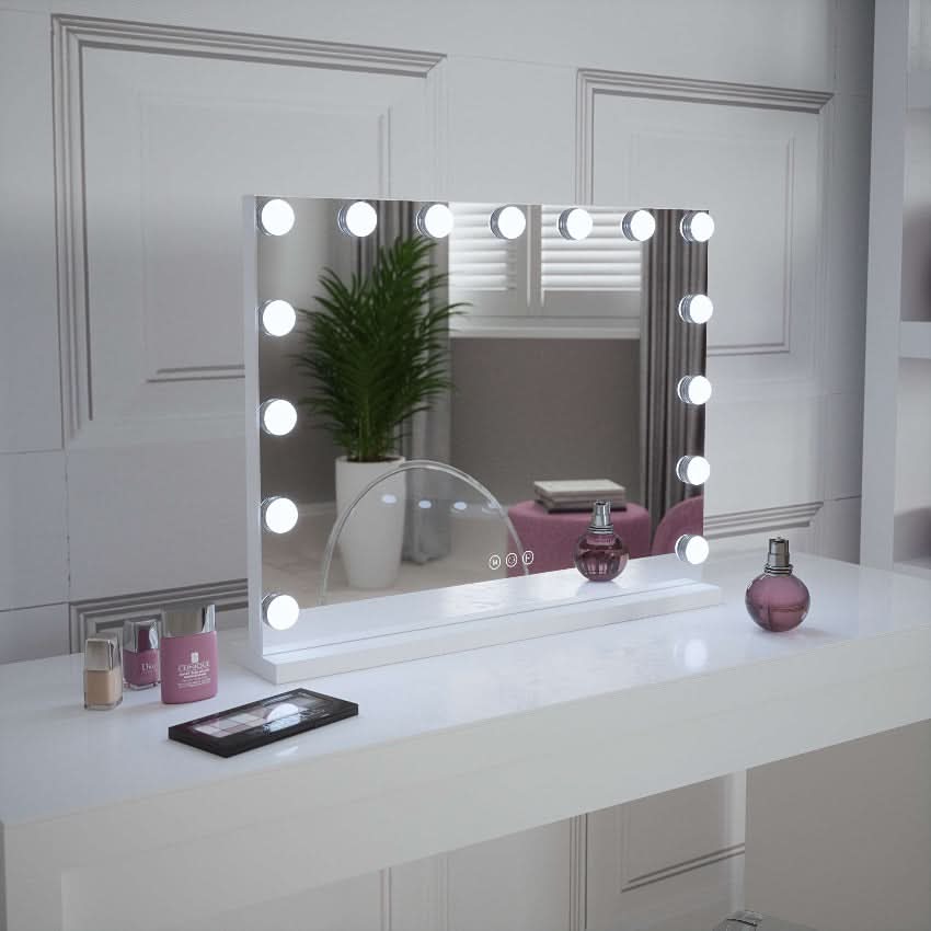 The Jessica Hollywood Mirror 58cmX46cm with round LED bulbs sits on a white desk, surrounded by pink and beige cosmetic bottles, an eyeshadow palette, and a potted plant near a window for versatile chic lighting.